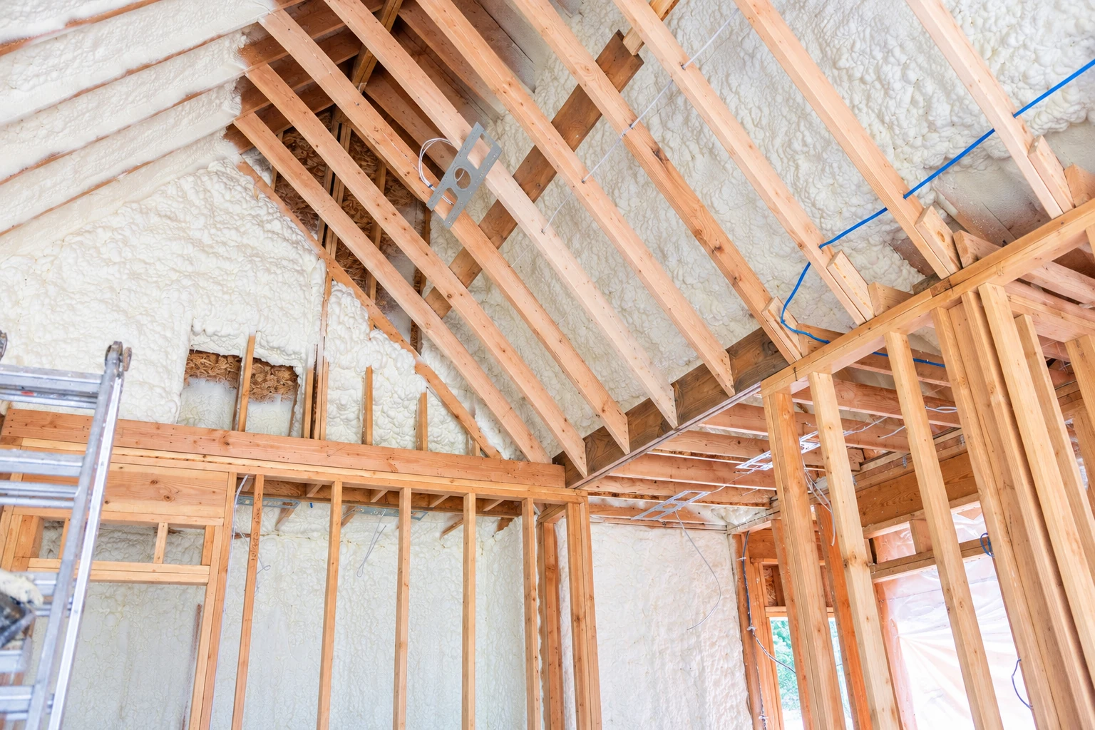 Attic framing with exposed wooden rafters and thick white spray foam covering the roof slopes and walls.