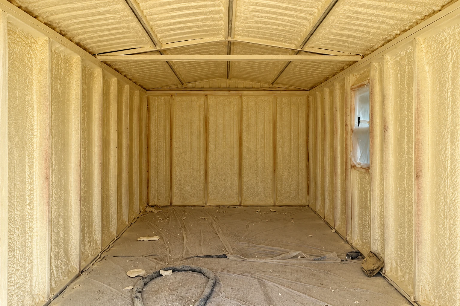 Empty framed room with yellow spray foam insulation coating the walls and ceiling.
