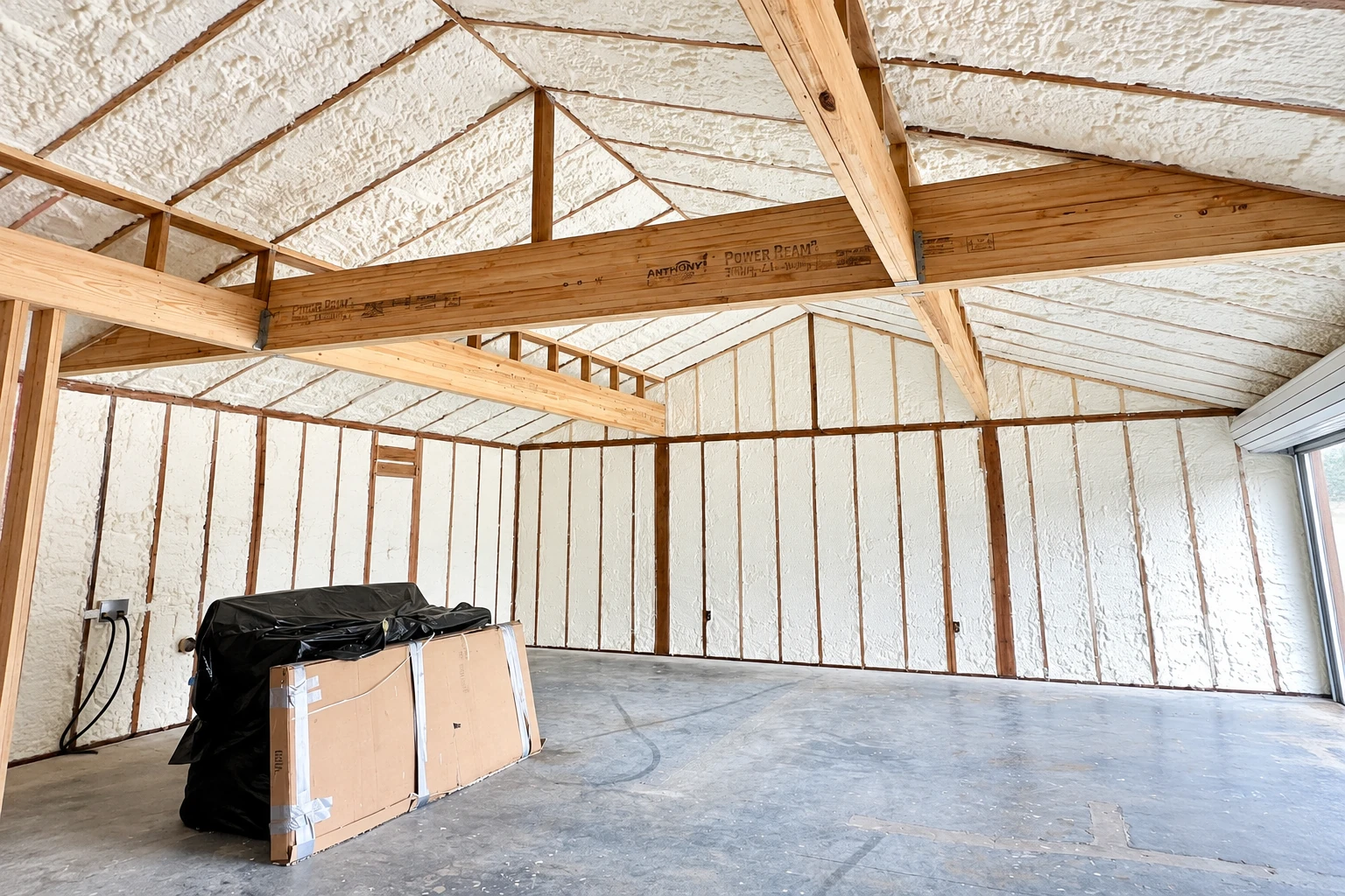 Unfinished room with white spray foam insulation covering the walls and pitched ceiling between exposed wooden framing.