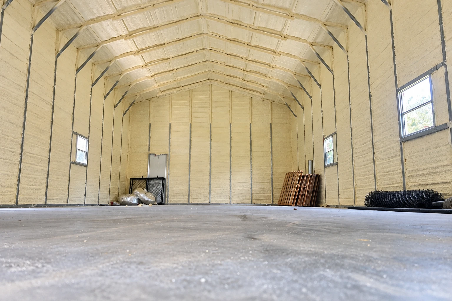 Large interior space with pale spray foam coating the walls and arched ceiling around metal supports and windows.